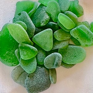 May include: A collection of smooth, sea-green glass pieces, likely sea glass, with a variety of shapes and sizes. The glass has a frosted, textured appearance.