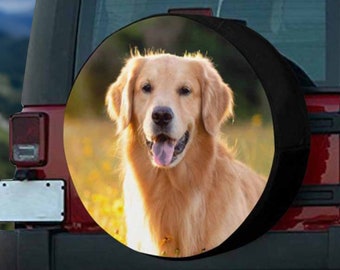 May include: A black spare tire cover with a golden retriever dog printed on it. The dog is looking directly at the camera with its tongue sticking out. The background is a blurry field of yellow flowers.