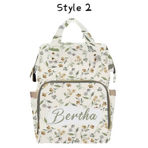 May include: A white diaper bag with a floral pattern and a personalized name tag that says "Bertha".