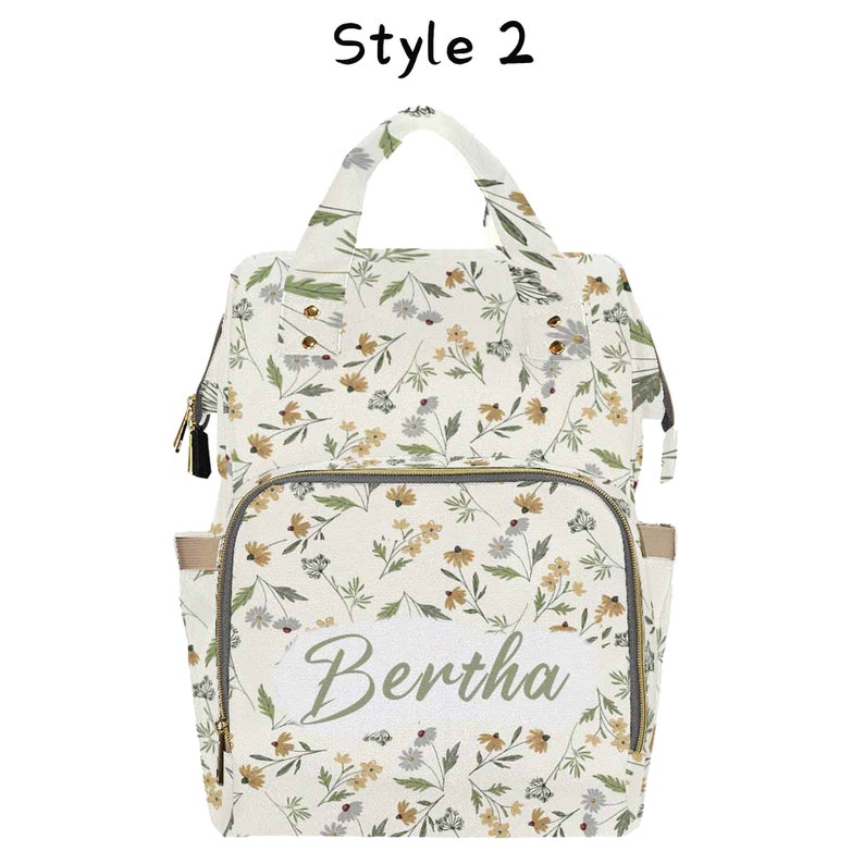 May include: A white diaper bag with a floral pattern and a personalized name tag that says "Bertha".