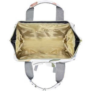 May include: An open white canvas tote bag with a floral print. The bag has a zipper closure and multiple interior pockets. The bag has two top handles and two adjustable shoulder straps.