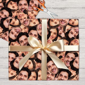 May include: A gift wrap featuring a repeating pattern of faces. The faces are a mix of men and women, and they are all smiling. The wrapping paper is tied with a gold ribbon.