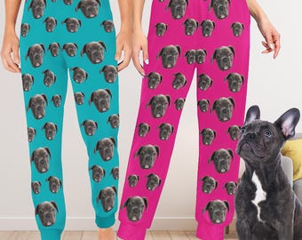 May include: Two pairs of blue and pink pyjama trousers with a repeated pattern of a dog's face. A black French bulldog is sitting on the floor in front of the trousers.