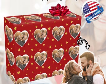 May include: Red wrapping paper with a repeating pattern of gold glitter hearts and a couple's photo in a heart-shaped frame. The text "Custom Wrapping Paper" is at the top of the image. A small American flag with the text "Made in America" is in the upper right corner.