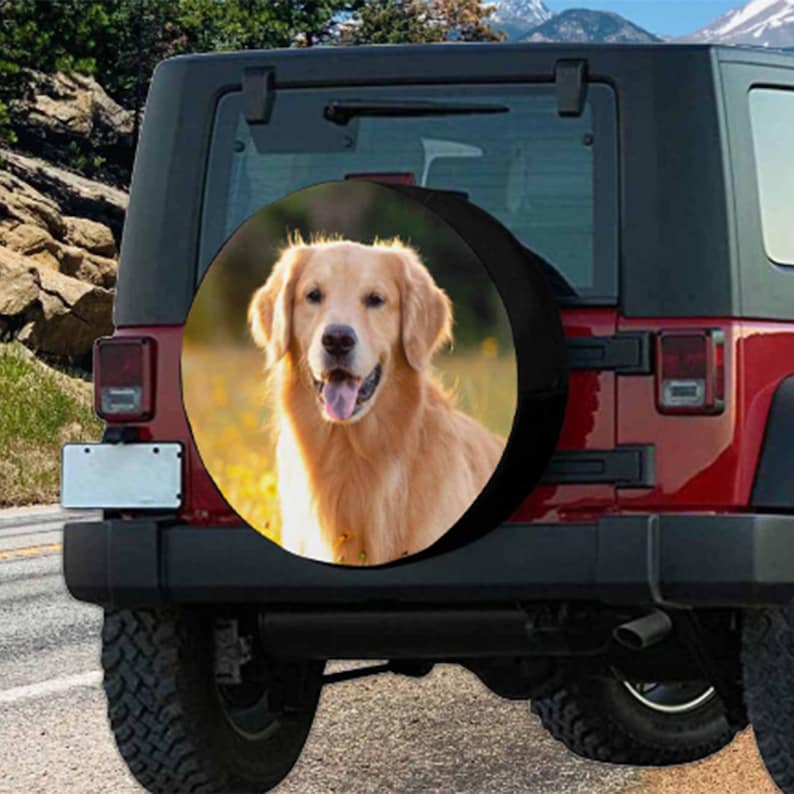 May include: A red Jeep with a spare tire cover featuring a golden retriever dog. The dog is looking directly at the camera with its tongue sticking out. The tire cover is black with a white border.