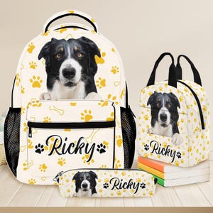 May include: A matching set of school supplies featuring a black, white, and brown dog. The set includes a backpack, lunch bag, and pencil case, all with a repeating pattern of yellow paw prints and bones. The name "Ricky" is printed on each item.