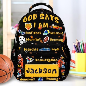 May include: Black backpack with the text "GOD SAYS I AM" and positive affirmations. Features a yellow name tag with "Jackson" in blue. Includes sports and car graphics.