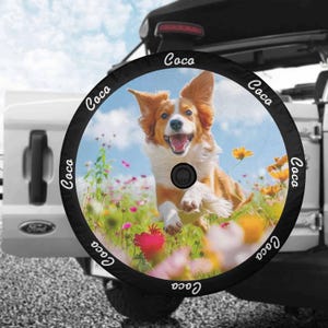 May include: Black spare tire cover with a white border and the word "Coco" repeated around the edge. The center of the cover features a colorful image of a dog running through a field of flowers.