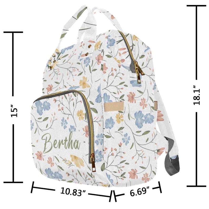 May include: A white diaper bag with a floral pattern in shades of blue, pink, and yellow. The bag has a large main compartment, a front pocket with the name "Bertha" embroidered on it, and adjustable straps. The bag measures 18.1 inches tall, 10.83 inches wide, and 6.69 inches deep.