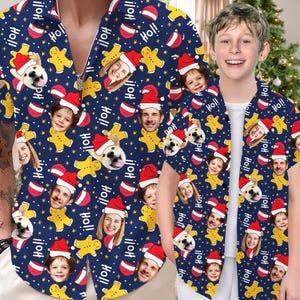 May include: Two blue short-sleeved shirts with a Christmas theme. The shirts feature a repeating pattern of gingerbread men, Santa hats, stars, and the word "Ho!!".  Each shirt has a different pattern of faces.