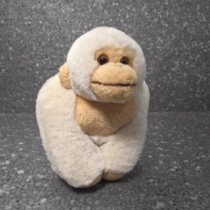 Può includere: Un peluche a forma di gorilla con corpo color crema e viso, petto e orecchie color beige. Il gorilla ha occhi marrone scuro e una bocca cucita. Il giocattolo è progettato per stare seduto e ha una consistenza morbida e sfocata.