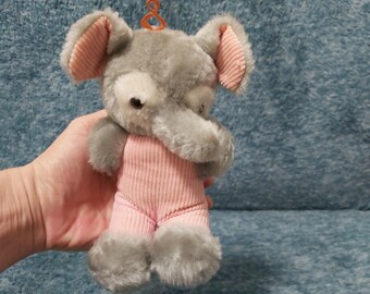May include: A gray plush elephant wearing a pink corduroy onesie. The elephant has a small, pink, corduroy nose and ears.