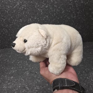 Op de afbeelding: Een kleine, crèmekleurige pluche ijsbeer met zachte, gestructureerde vacht, afgeronde oren en een zwarte neus. Het knuffeldier wordt in zijaanzicht weergegeven, waarbij de compacte, ronde lichaamsvorm en realistische gelaatstrekken zichtbaar zijn.