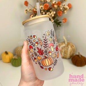 May include: A frosted glass tumbler with a bamboo lid and a clear straw, featuring a colourful heart-shaped graphic composed of autumn-themed illustrations including pumpkins, acorns, mushrooms, and various fall leaves in shades of orange, red, and yellow.