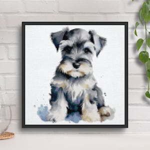 Peut inclure: Une broderie au point de croix de style aquarelle encadrée représentant un chiot Schnauzer. L'œuvre présente le chien dans des tons de gris, de blanc et de beige, avec un effet doux et pictural. Le chiot est assis, sur fond blanc.