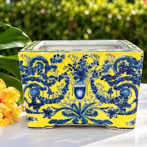 May include: A rectangular ceramic planter featuring a bright yellow background with intricate blue floral and scrollwork patterns. The design includes a central urn motif surrounded by symmetrical botanical elements and decorative flourishes.