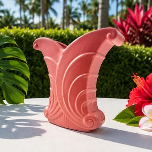 May include: A coral pink ceramic vase featuring a wide, flared opening with curled edges and a series of vertical, curved ridges along the body. The vase has a symmetrical, fan-like shape with a solid base and a smooth, glossy finish.
