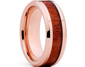 May include: A rose gold tungsten carbide ring with a brown wood inlay. The ring has a beveled edge and a polished finish.