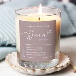 Puede incluir: Un tarro de vidrio para velas con una etiqueta marrón claro que dice "IN LOVING MEMORY OF Wana (1959-2022)". La etiqueta también incluye el texto "Your life was a blessing your memory a treasure... You are loved beyond words and missed beyond measure..."