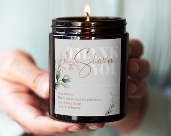 May include: A brown glass candle with a white label that says "Thank Sharon You". The label also has a handwritten message that says "Dear Sharon, Thank you so much for everything you've done for us! Love Ali & Tom xx".