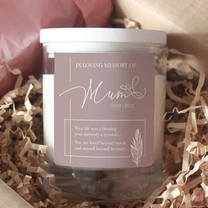 May include: A glass candle jar with a white lid and a brown label. The label says "In loving memory of Mum (1959-2022)" and includes a quote: "Your life was a blessing, your memory a treasure... You are loved beyond words and missed beyond measure..."