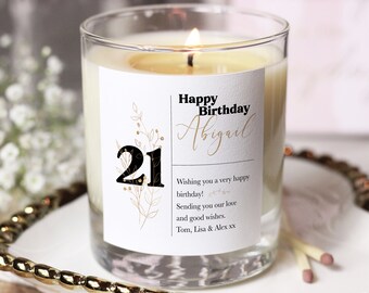 Puede incluir: Una vela blanca con una etiqueta negra que dice "Happy Birthday Abigail" y "21". La etiqueta también incluye un diseño floral y el mensaje "Wishing you a very happy birthday! Sending you our love and good wishes. Tom, Lisa & Alex xx".