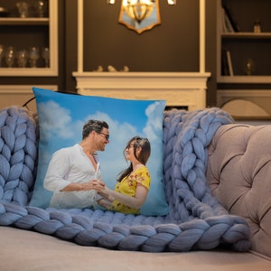May include: A throw pillow featuring a photograph of a couple smiling at each other on a beach. The image is printed on a white pillowcase with a blue background.