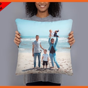 Op de afbeelding: Een gezin van vier op een strand, de ouders houden hun twee kinderen vast, één op elke schouder. Het gezin draagt ​​casual kleding en glimlacht. Het strand is zanderig met blauw water op de achtergrond.
