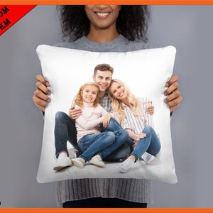 May include: White cushion with a printed image of a family of three. The family are sitting on a white background and smiling. The father is wearing a blue shirt and jeans, the mother is wearing a striped shirt and jeans, and the daughter is wearing a pink shirt and jeans.