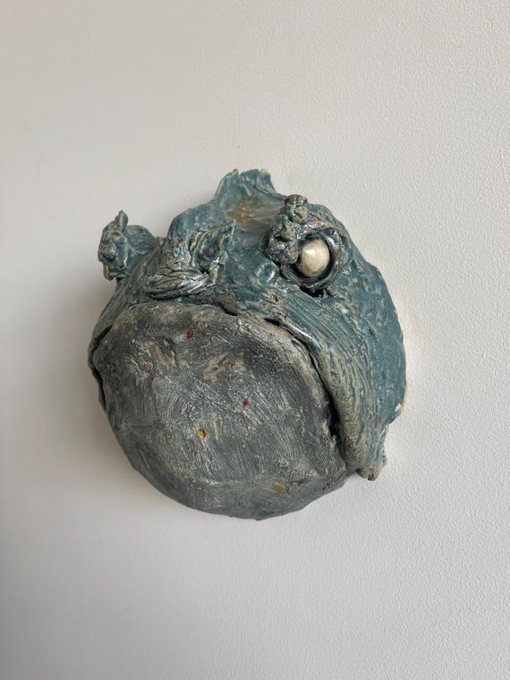 A handmade ceramic swamp creature mounted on a wall — part sculpture, part character study, 100% something you've never seen at HomeGoods.