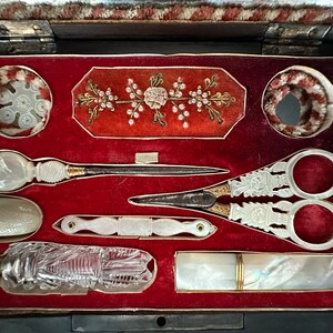 Pu&ograve; includere: Un kit da cucito vintage con un interno in velluto rosso. Il kit comprende un paio di forbici, un ago, un ditale, una piccola bottiglia e una piccola custodia. Il kit &egrave; decorato con un motivo floreale.