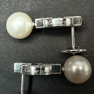 May include: Two silver earrings with a pearl and a diamond-encrusted design. The earrings are marked 'Cartier 750' on the back.