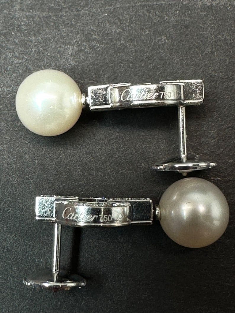 May include: Two silver earrings with a pearl and a diamond-encrusted design. The earrings are marked 'Cartier 750' on the back.