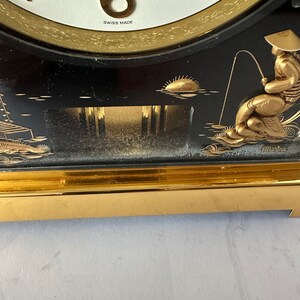 Puede incluir: Un reloj negro y dorado con un borde dorado y un dise&ntilde;o de pescador. La esfera del reloj es blanca con n&uacute;meros romanos negros y las palabras "Swiss Made".
