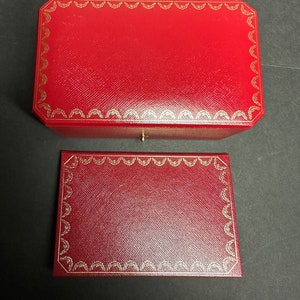 May include: Two red leather boxes with gold trim. The top box is slightly larger than the bottom box. Both boxes have a repeating pattern of gold crescents around the edges.