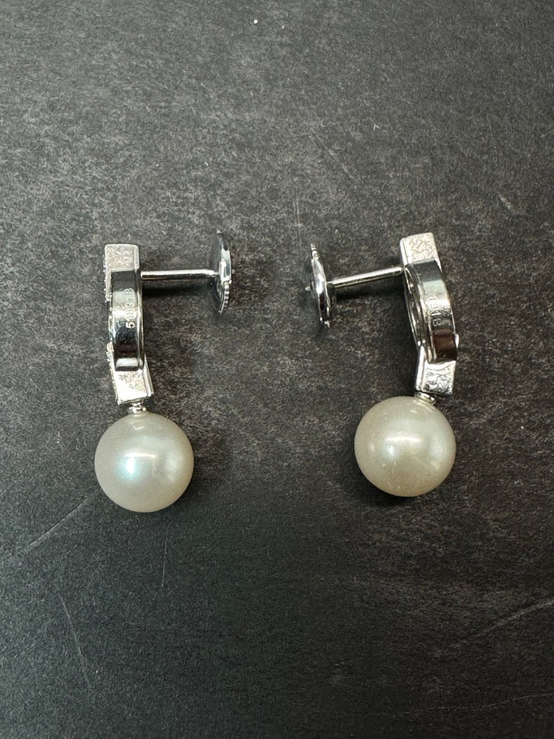 May include: A pair of silver earrings with a pearl drop and a small diamond-like design on the top. The earrings are on a gray surface.