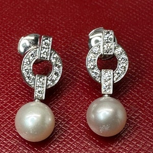 May include: A pair of silver earrings with a pearl drop and a diamond encrusted circle design.