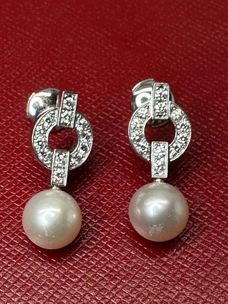 May include: A pair of silver earrings with a pearl drop and a diamond encrusted circle design.