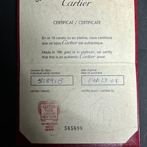 May include: A tan certificate with a red border. The text on the certificate reads: 'Cartier', 'Certificat / Certificate', 'En or 18 carats ou en platine, nous certifions que ce bijou Cartier est authentique.', 'Made in 18K gold or in platinum, we certify that this is an authentic Cartier jewel.', 'Numéro du bijou', 'Individual serial number', '51891B', 'Cachet / Stamp', 'Date d'achat', 'Date of purchase', 'Feb 13-07', 'Certifié exact / Certified by'. The certificate also has a stamp that reads: 'Cartier', 'Paris', 'London', 'New York', '600 Pine Street', 'Seattle', 'WA. 98101', and '585898'.