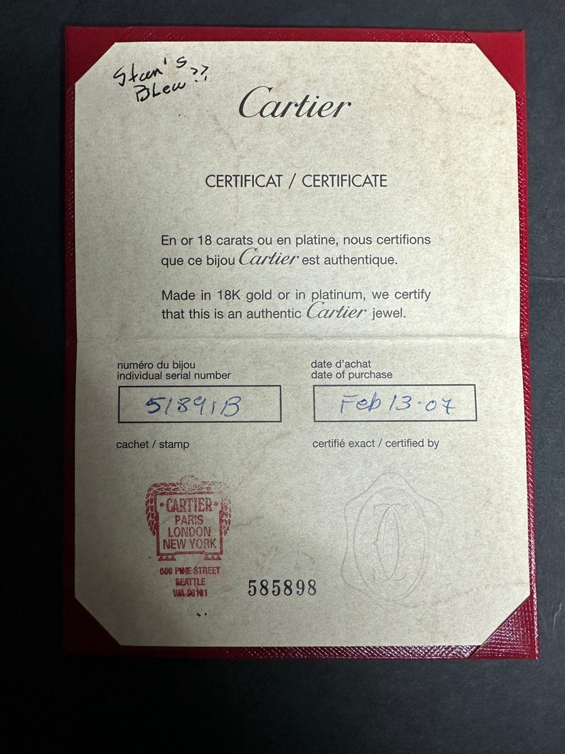 May include: A tan certificate with a red border. The text on the certificate reads: 'Cartier', 'Certificat / Certificate', 'En or 18 carats ou en platine, nous certifions que ce bijou Cartier est authentique.', 'Made in 18K gold or in platinum, we certify that this is an authentic Cartier jewel.', 'Numéro du bijou', 'Individual serial number', '51891B', 'Cachet / Stamp', 'Date d'achat', 'Date of purchase', 'Feb 13-07', 'Certifié exact / Certified by'. The certificate also has a stamp that reads: 'Cartier', 'Paris', 'London', 'New York', '600 Pine Street', 'Seattle', 'WA. 98101', and '585898'.