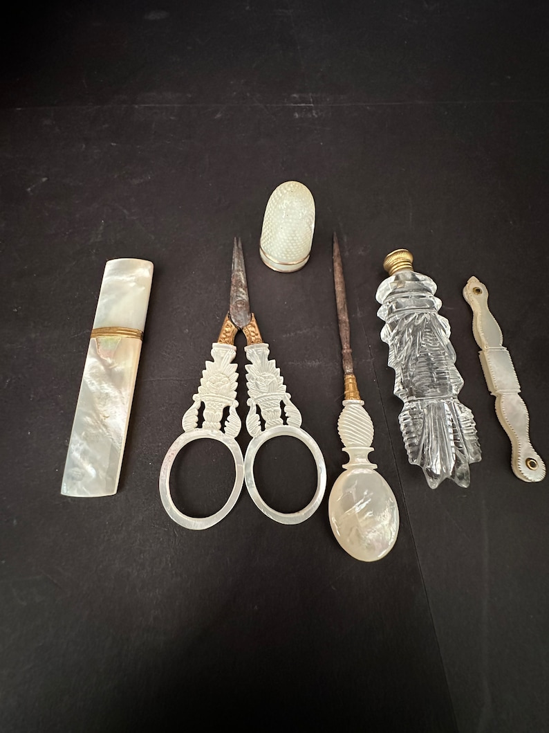 Pu&ograve; includere: Un set di strumenti da cucito vintage in madreperla e vetro. Il set comprende un ditale, delle forbici, un infila-ago, un astuccio per aghi e una piccola bottiglia.