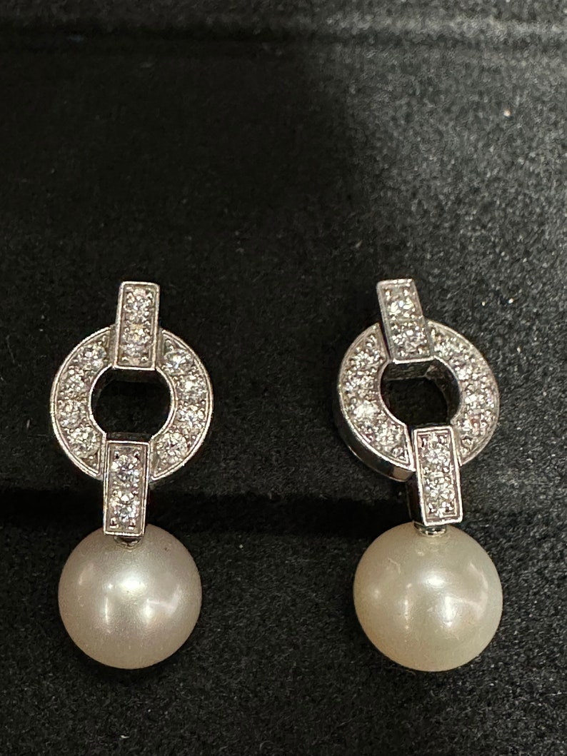 May include: A pair of silver earrings with a pearl drop and a diamond circle design.