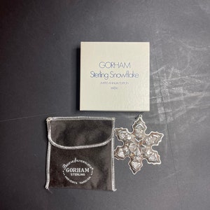 May include: A silver snowflake ornament in a velvet pouch with the text "Pacific Silvercloth Gorham Sterling Prevents Tarnish" and a box with the text "Gorham Sterling Snowflake Limited Annual Edition #9/250".