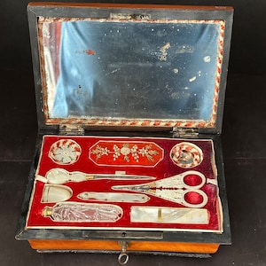 Pu&ograve; includere: Uno scrigno da cucito in legno antico con interno in velluto rosso. Lo scrigno contiene una variet&agrave; di strumenti da cucito, tra cui forbici, un infila-ago, un ditale e una piccola bottiglia. Lo scrigno ha un piccolo buco della serratura e una chiave.