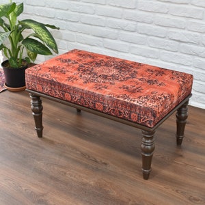 May include: A wooden bench with a red and black patterned cushion. The bench has turned legs and a rectangular top.