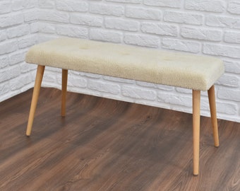 May include: A white upholstered bench with four wooden legs. The bench is sitting on a wood floor.
