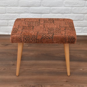 May include: A brown and black patterned ottoman with wooden legs. The ottoman is sitting on a wooden floor.