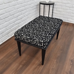 Puede incluir: Banco con estampado en blanco y negro con patas de madera negra. El banco está sobre un suelo de madera oscura.