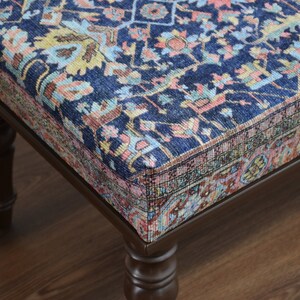 May include: A dark blue ottoman with a patterned fabric top and dark brown wooden legs.