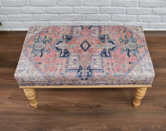 Puede incluir: Un otomano de madera con patas torneadas y una parte superior de tela estampada en rosa, azul y blanco.